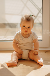 一个 7 个月大的女孩穿着紧身连衣裤坐在家里的阳台门附近