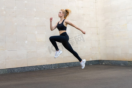 运动和健身概念年轻成年白人女运动员跳高户外灰色尾巴墙背景