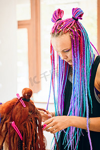 头爆炸摄影照片_扎着彩色爆炸式辫子的美发师正在编织姜黄色长发绺。