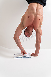 健美运动员在他的头底部孤立的白色背景上阅读这本书，男性书男子气概，白人光着膀子，知识分子站立。 