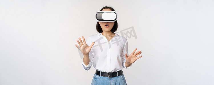 虚拟现实中惊奇的年轻女性，使用 vr 眼镜耳机，站在白色背景上