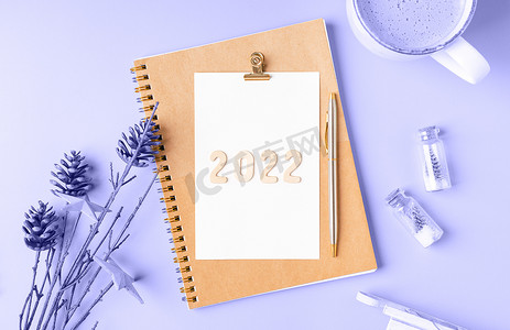 紫色桌面摄影照片_顶部视图桌面圣诞记事本，带有 2022 年颜色的文本。