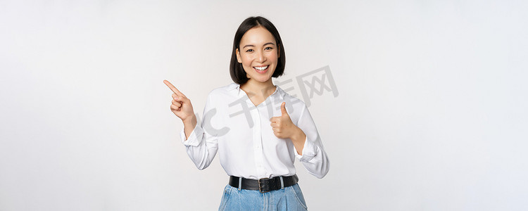 年轻亚洲女商人的形象，微笑着向左指指点点，竖起大拇指，推荐产品，赞美，站在白色背景上