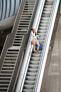 带着旅行包和手机站在自动扶梯上的快乐非洲裔美国女性