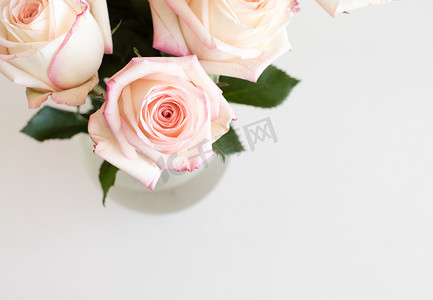 白桌上玻璃花瓶中粉色和奶油色玫瑰的高角度视图（裁剪和选择性焦点）