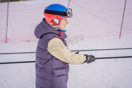 爬山冬天摄影照片_女滑雪者在初学者的滑雪缆车上爬山