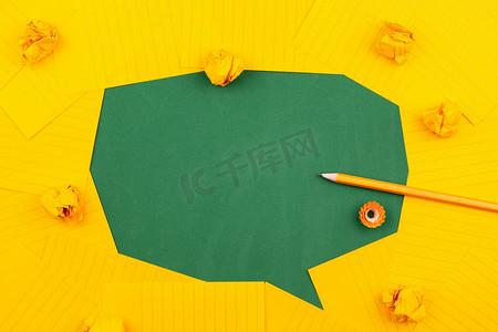橙色对话框摄影照片_橙色的纸片放在绿色的学校董事会上，用铅笔、弄皱的纸和文本的复制空间形成一个聊天气泡。