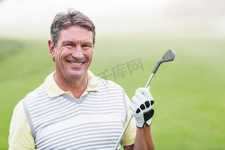 快乐的高尔夫球手拿着他的球杆对着镜头微笑