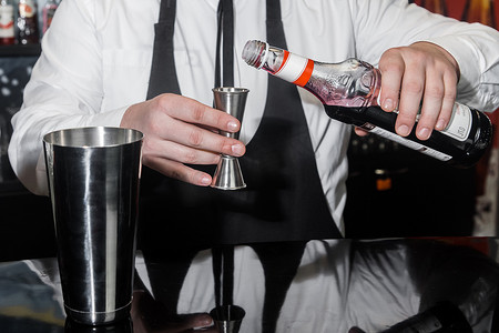 专业酒保的手将红糖浆倒入量杯中，旁边是一个金属工具，用于准备和搅拌振动器饮料的酒精鸡尾酒