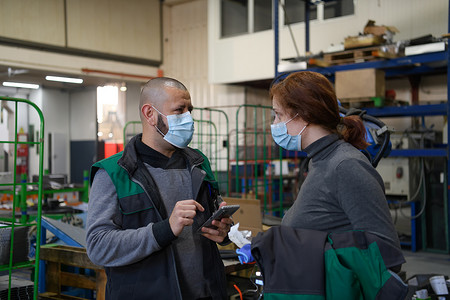 戴着面罩防止日冕病毒的工业工人讨论工厂生产。