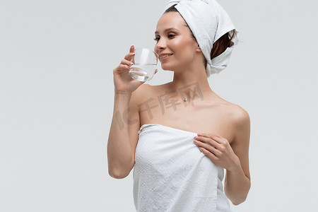 纯净水摄影照片_自信放松的女人，头上戴着白毛巾，喝着纯净水，看着别处