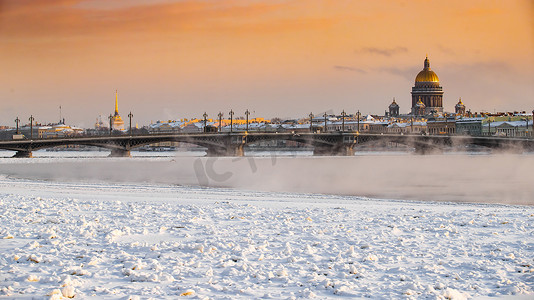 城市河流摄影照片_日落时圣彼得堡的冬季全景，以撒大教堂和 Blagoveshenskiy 桥为背景，冰冻的涅瓦河上的蒸汽，橙色的天空