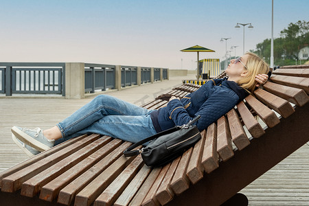 空荡荡的城市路堤上的年轻女子躺在日光躺椅上