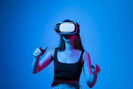 年轻女孩使用 VR 眼镜玩游戏，享受虚拟现实耳机，同时在霓虹灯下与 metaverse 中的朋友玩游戏。
