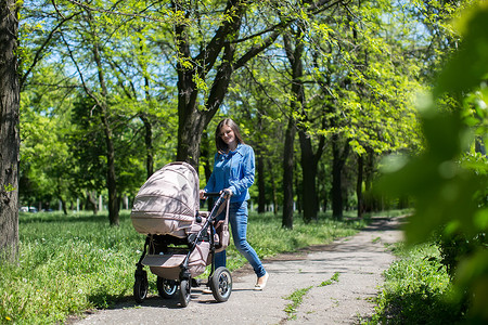 年轻的妈妈在公园里推着婴儿车走路。