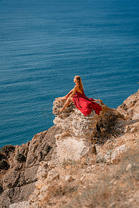 一位身穿红色长裙、头发飘逸的女孩坐在海面上的岩石上。