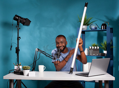 视频博客评论员在视频博客工作室中展示 RGB 管视频灯，坐在办公桌前，配有笔记本电脑