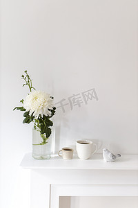 玻璃花瓶中的大菊花、两杯带凹槽的咖啡和桌上的陶瓷小鸟雕像。