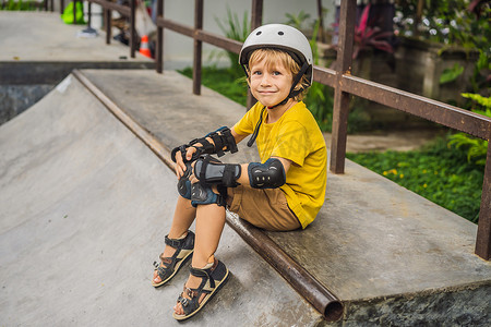 戴着头盔和护膝的运动男孩在滑板公园里学习滑板。