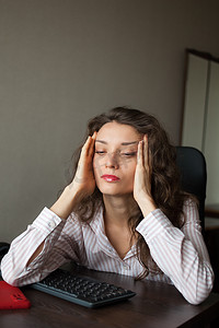 一头卷发和白衬衫的疲惫的年轻女性正在办公室使用她的笔记本电脑、日常工作、自由职业者、倦怠综合症