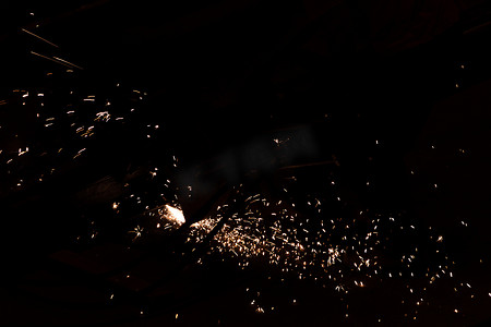 工人使用切割机切割金属，在弱光下聚焦锋利火花的闪光线