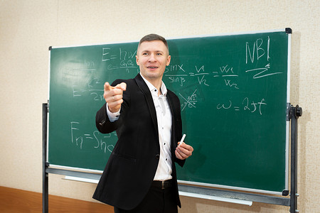 男老师在课堂上用白色粉笔在黑板上写字给学生上课