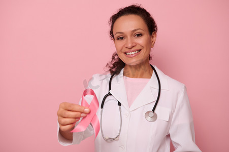 国际卫生组织摄影照片_华丽的非洲裔美国女医生，有着美丽的露齿微笑，展示着一条粉红色缎带，隔离在彩色背景上，有复制空间。
