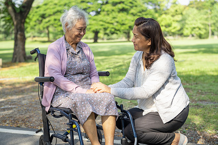 坐在椅子上的人摄影照片_看护者帮助和照顾亚洲老年或老年老妇人病人坐在公园的轮椅上，快乐地坐在轮椅上，健康强大的医疗理念。