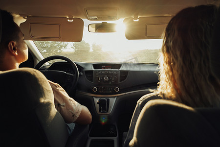 女人和男人乘汽车旅行的后视图，年轻夫妇在日落时的公路旅行