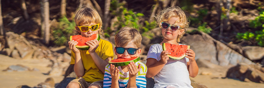 孩子们戴着太阳镜在沙滩上吃西瓜横幅，长版
