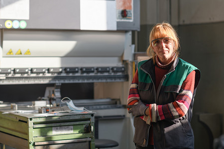 一位戴着护目镜站在数控机床前，在现代化金属生产加工厂工作的女性肖像