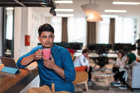 休闲商人在现代开放式创业办公室的休闲区喝茶时使用笔记本电脑从工作中休息