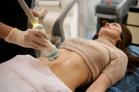 特写触摸超声波传感器在接触凝胶润滑的腹部上移动，模糊的女人在水疗诊所接受身体轮廓空化治疗。