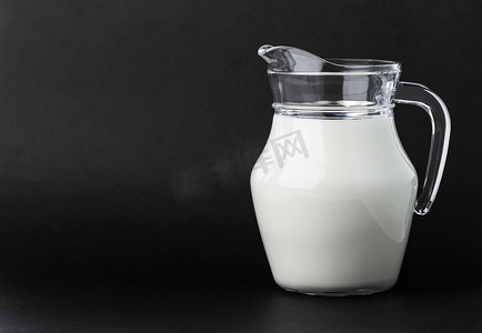 牛奶玻璃壶摄影照片_黑色背景的玻璃壶牛奶，带复制空间
