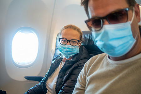 一对年轻夫妇在乘飞机旅行时戴着口罩。 