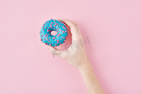 女人手拿粉红色背景上的彩色甜甜圈。