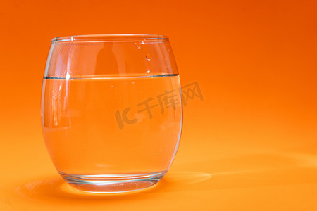 橙色渐变背景上装有纯净水的玻璃杯。