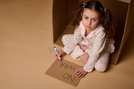 穿着睡衣的顶视图小女孩坐在纸板箱里，在海报上写着没有战争，躲避军事和政治冲突。