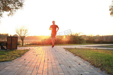 跑步运动的人摄影照片_运动的年轻人在户外跑步以保持健康，在日落或日出。