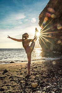 女子体操运动员正在海边夕阳的沙滩上训练。