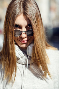 一个戴着墨镜走在街上的现代女孩戴着耳机听音乐。