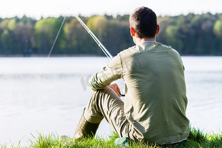 钓鱼者坐在湖边的草地上，拿着鱼竿钓鱼