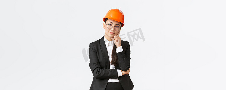 微笑的亚洲职业女商人投资建设，管理企业工作，戴着安全帽和西装，看着镜头很高兴，站在白色背景