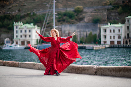 红堤摄影照片_身着红裙的女子，长着丝绸长翅膀的时装模特，身着飘逸的裙子，在堤岸上飞舞着布料。