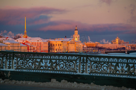 日落时圣彼得堡的冬季全景，彼得和保罗要塞的金色尖顶，Kunstkamera 塔，背景有桥的堤坝，结冰的涅瓦河上的蒸汽，橙色的天空