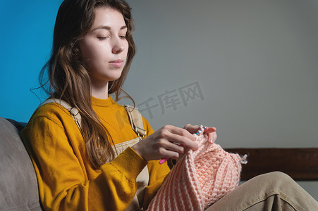 年轻快乐的白种女人微笑着坐在沙发上，钩编羊毛产品。