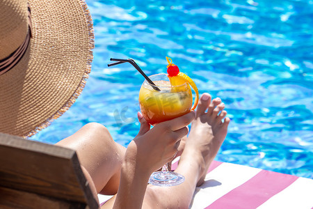 泳池边日光躺椅上的女孩喝着鲜榨橙子调制的鸡尾酒。