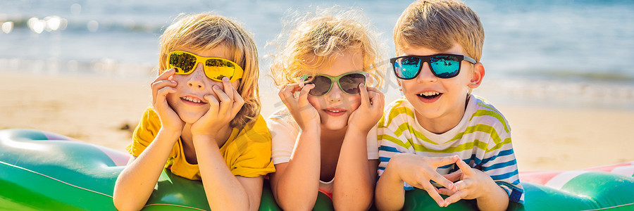 幸福banner摄影照片_孩子们坐在充气床垫上，戴着墨镜，背对着大海，玩得开心 BANNER, LONG FORMAT