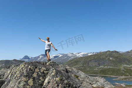 jotunheimen摄影照片_成年女性快乐地坐在岩石上，望着蓝色的海水