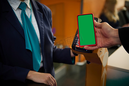 商务签到摄影照片_男性手持智能手机的特写，带有绿色色度键空白屏幕，带有移动应用程序和广告的复制空间，在机场通过航班登机牌时靠近银行终端